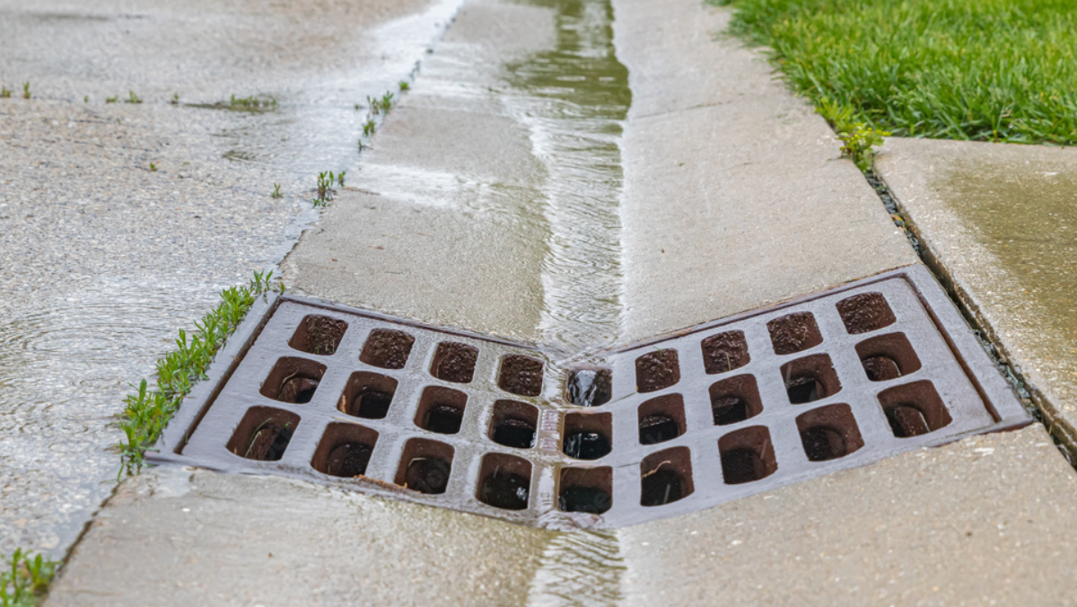 Stormwater drain grate capturing rainwater runoff along a concrete curb in a residential area